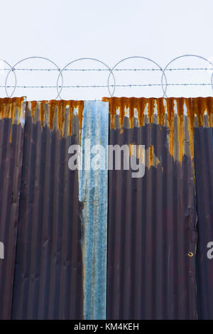 Usura di metallo ondulato, recinto di filo spinato sopra. Foto Stock