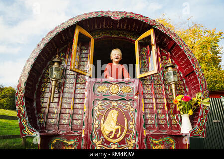 Un ragazzo sporgersi delle persiane aperte nella parte posteriore di un archetto top gypsy caravan. Foto Stock