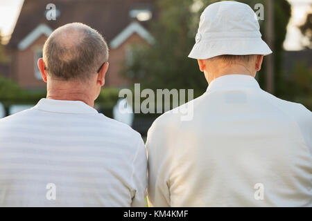 Due compagni, due uomini stavano in piedi a fianco a fianco in camice bianco all'esterno. prato giocatori di bocce, uno in un cappello per il sole. Foto Stock