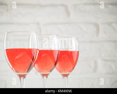 Tre wineglass con vino di colore rosa su bianco muro di mattoni in background Foto Stock