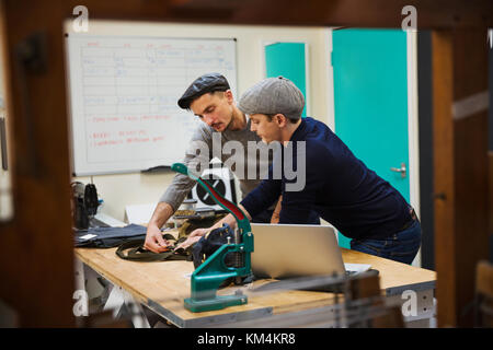 Due uomini, sarti appoggiata su un banco di lavoro per discutere un progetto, pianificare il loro lavoro. Foto Stock