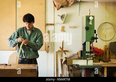 Un artigiano segnando un pezzo di legno curvo con una matita. Foto Stock