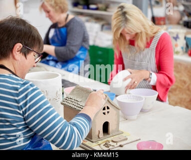 Un gruppo di persone sedute su un banco da lavoro in uno studio di ceramiche, decorare e modellare oggetti di creta. Foto Stock