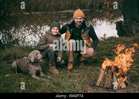 Padre e figlio seduti al falò Foto Stock