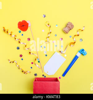 Scatola con fuoriuscite di coriandoli di nastro, luccica, paillettes, tizi, sughero, carta e altri accessori di festa sul colore giallo brillante background. flat laici minimi. Foto Stock