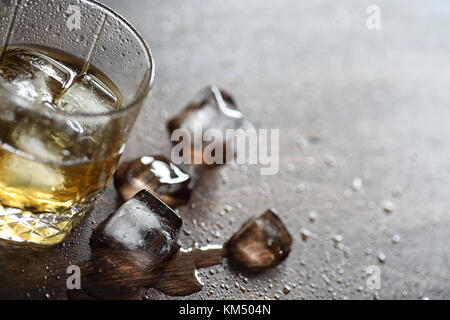 Whisky in un bicchiere e pezzi di ghiaccio su un legno Foto Stock