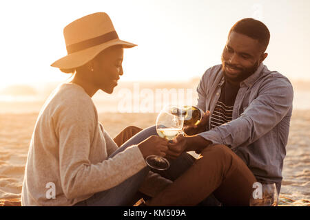 Sorridente coppia africana bevendo vino in spiaggia al tramonto Foto Stock