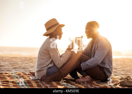 Giovane africano giovane bevendo vino in spiaggia al tramonto Foto Stock