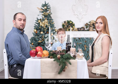 Ritratto di una famiglia di tre persone in una tavola festiva con l'albero di natale Foto Stock