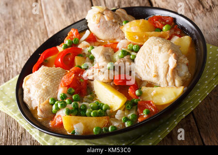 Pezzi di pollo in umido con patate e peperoni, pomodori, piselli e cipolle close-up in una ciotola sul tavolo orizzontale. Foto Stock