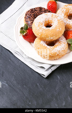 Piastra bianca di zucchero e ciambelle al cioccolato e fragole fresche servita su grigio tovagliolo tessili su tavola nera. Vedere serie Foto Stock