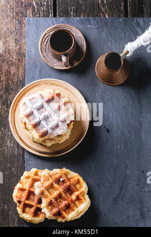 Piastra bianca in casa con cialde belghe con lo zucchero in polvere ceramica vuota tazza da caffè e vecchi cezve. su nero ardesia come sfondo. con copia spazio un Foto Stock