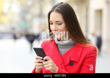 Grave donna utilizzando uno smart phone permanente sulla strada in inverno Foto Stock