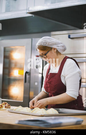 Donna adulta in occhiali e grembiule cuoce dolci al forno Foto Stock