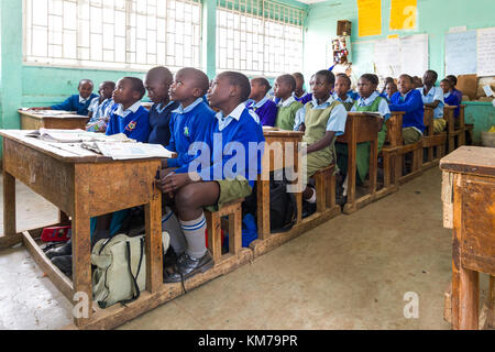 I bambini della scuola secondaria in uniforme si sedevano a banchi di legno ascoltando il loro insegnante durante la lezione, Nairobi, Kenya Foto Stock