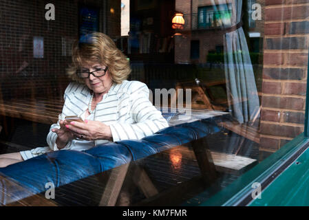 Londra, UK, elegante senior business donna controllando il suo telefono in un coffee shop, senior business donne Foto Stock