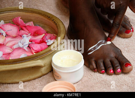Donna africana crema di spalmatura su i suoi piedi Foto Stock