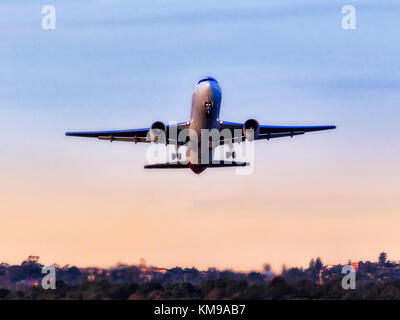 Passeggero moderno aereo in fase di decollo da aeroporto internazionale di Sydney contro il cielo blu e chiaro in vista di alberi di gomma e il quartiere residenziale. Foto Stock