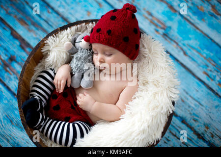 Little baby boy con maglia ladybug hat e pantaloni in un cestello, dormendo pacificamente in un cestello, isolato studio shot Foto Stock