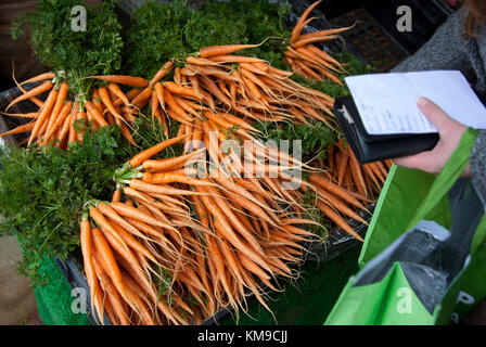 Una donna con una lista della spesa sceglie le carote su una bancarella di verdure al pluripremiato mercato agricolo di Stroud, Gloucestershire, Regno Unito Foto Stock