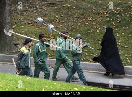 Una donna iraniana indossa un chador mentre passa davanti a tre lavoratori con pale in un parco di Teheran, il 23 novembre 2017. | utilizzo in tutto il mondo Foto Stock