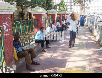 Uomo che trasportano il sacco sulla spalla e camminare davanti agli uomini seduti sul muro di cinta a Mysore, mysuru, Karnataka, India. Foto Stock