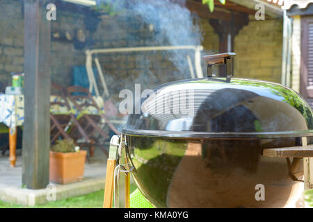 Il fumo uscire da un barbecue chiuso durante la tirata grigliate di carne di maiale Foto Stock