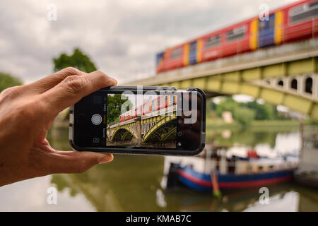 Un maschio di scattare foto di Richmond ponte ferroviario (Grade II) struttura con il suo iPhone SE, Londra Foto Stock