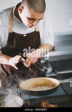 Giovane maschio attraente cook con uniforme di preparare piatti deliziosi. Foto Stock