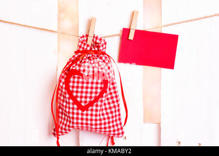 Gifting Tema immagine con un tessuto a scacchi la sacca e una decorazione cuore rosso e un messaggio vuoto card, legata ad una stringa con clip in legno. Foto Stock