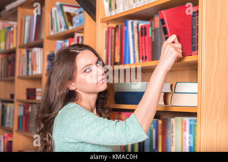 Istruzione Tema immagine con una bella ragazza di prendere un libro da una libreria per studiare o godendo di un romanzo nel tempo libero. Foto Stock