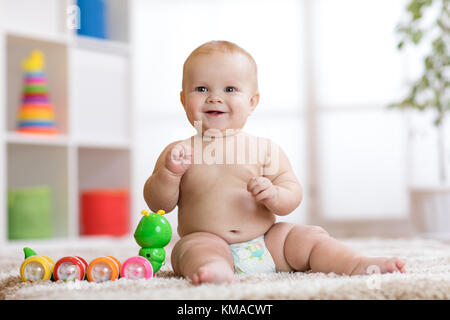 Adorabili poco baby nel pannolino si siede sul tappeto e gioca con il giocattolo a casa. profondità di campo. Foto Stock