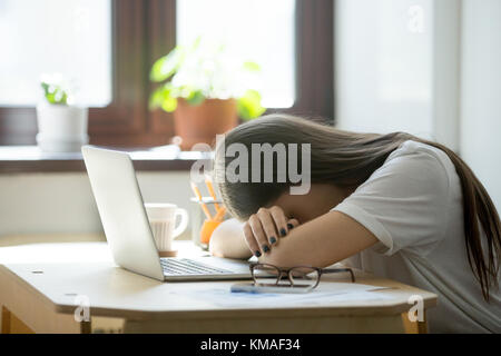 Giovane donna stanca che si addormenta alla scrivania dopo il lavoro eccessivo. Il sonno esausto privava la direttrice stressata che sdraiava sul tavolo e dormiva dopo un duro lavoro Foto Stock