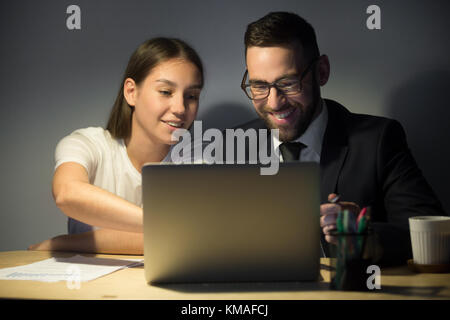 Bella giovane lavoratore di sesso femminile che discutendo di domanda di lavoro con un collega e dispositivo di puntamento su schermo portatile. millenaria happy businessman barbuto in bicchieri l Foto Stock