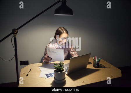 La millenaria imprenditrice guardando sullo schermo del computer portatile e confrontando i nuovi dati con business plan. superlavoro, overhours, scadenza, turno di notte concetto in Foto Stock