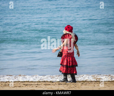 Donna anziana che indossa un abito di flamenco rosso a pois che cammina sulla spiaggia in spagna Foto Stock