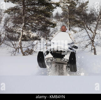 L'uomo adulto salta con una motoslitta nella neve sulla montagna in Norvegia Foto Stock