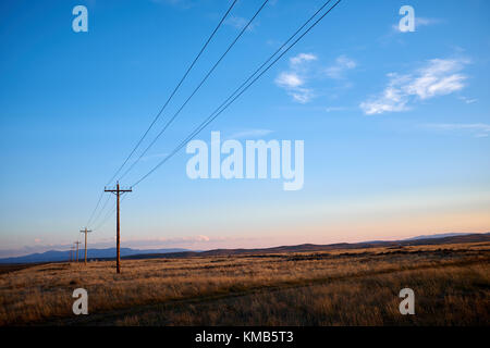 Fila di pali dell'elettricità con i cavi ad alta tensione in una vista in recessione in aperta campagna in North Park, COLORADO al tramonto con il bagliore arancione sul Foto Stock