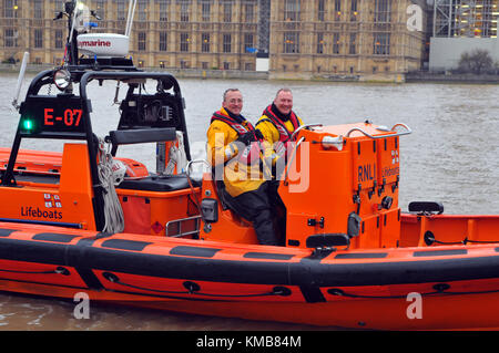 Due del volontario equipaggio sul Tamigi scialuppa di salvataggio a Londra seduti in barca con le case del parlamento in background. RNLI le imbarcazioni di salvataggio di Londra. Foto Stock