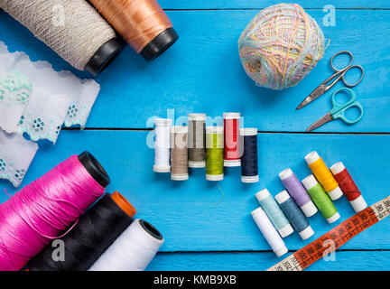 Colorata per cucire gli steli di linea, grandi e piccole, forbici, balza di panno morbido e nastro di misurazione sulla parte superiore di un blu sullo sfondo di legno piano portapaziente, concept Foto Stock