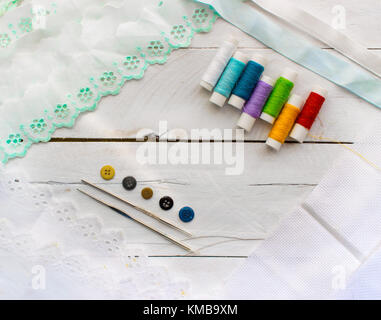 Filettatura stelo e colorati di filati per cucire le linee, aghi metallici e shirt pulsanti, con balza di panno morbido sulla parte superiore di un bianco sullo sfondo di legno, centrato Foto Stock