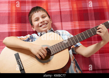 Ragazzo la riproduzione di musica di chitarra, giace su un rosso a scacchi blanket, vista dall'alto Foto Stock