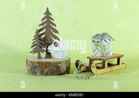 Una miniatura in legno portante della slitta in un piccolo regalo accanto a una decorazione albero di Natale fatto di legno con un piccolo scoiattolo su uno sfondo verde Foto Stock