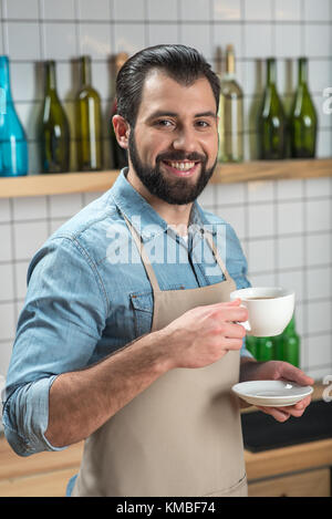 Sorridente giovane cameriere una buona sensazione mentre si beve il caffè sul posto di lavoro Foto Stock