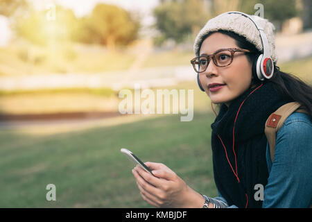 Asia ragazza apprendimento dello studente ascolto tutorial audio in un parco di seduta sul prato in un parco. Foto Stock