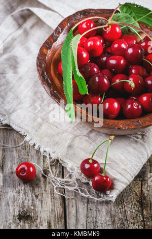 Ciotola di legno di ciliegie fresche con foglie sul vecchio tavolo in legno Foto Stock