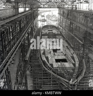 Degli anni Cinquanta, foto storiche di una nave in costruzione in un bacino a secco sotto il gantry Arrol presso la famosa Harland e Wolff, in cantiere dove il Titanic e altri grandi Olympic-le navi di classe sono stati costruiti, Belfast, Irlanda del Nord. Foto Stock