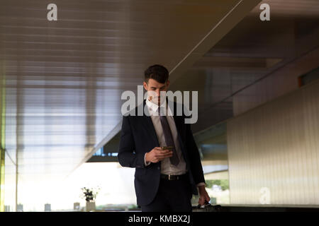 Imprenditore texting con smart phone nella lobby di office Foto Stock