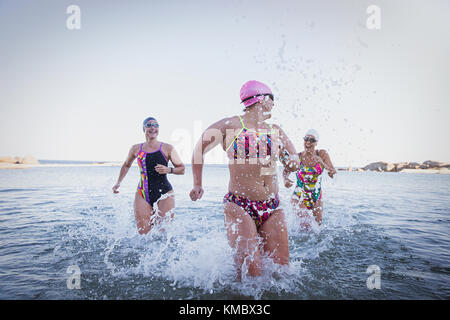 Nuotatori femminili in acqua aperta che corrono, che spruzzano nel surf dell'oceano Foto Stock