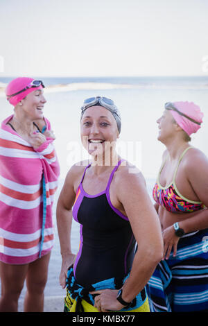 Ritratto sorridente, sicuro nuotatori d'acqua aperta femmina che si asciugano con asciugamani in oceano Foto Stock